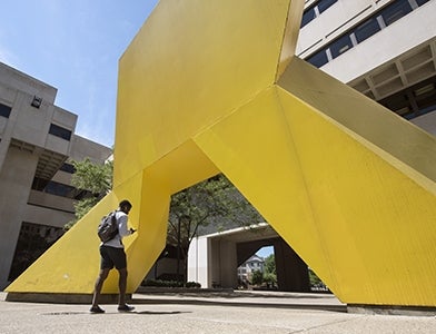 student walking toward large yellow sculpture